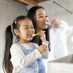 little girl with mom brushing teeth in bathroom, korean woman helping to brush daughter's teeth at home together