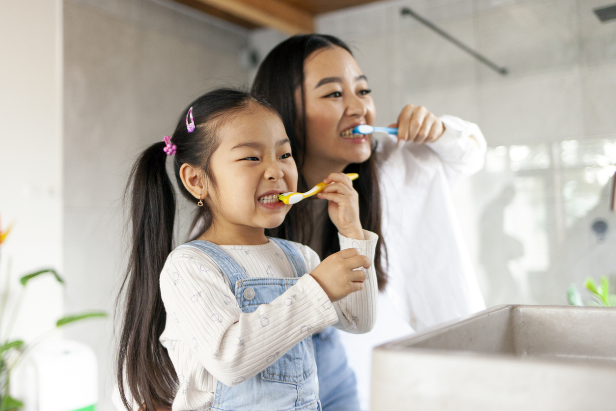 little girl with mom brushing teeth in bathroom, korean woman helping to brush daughter's teeth at home together